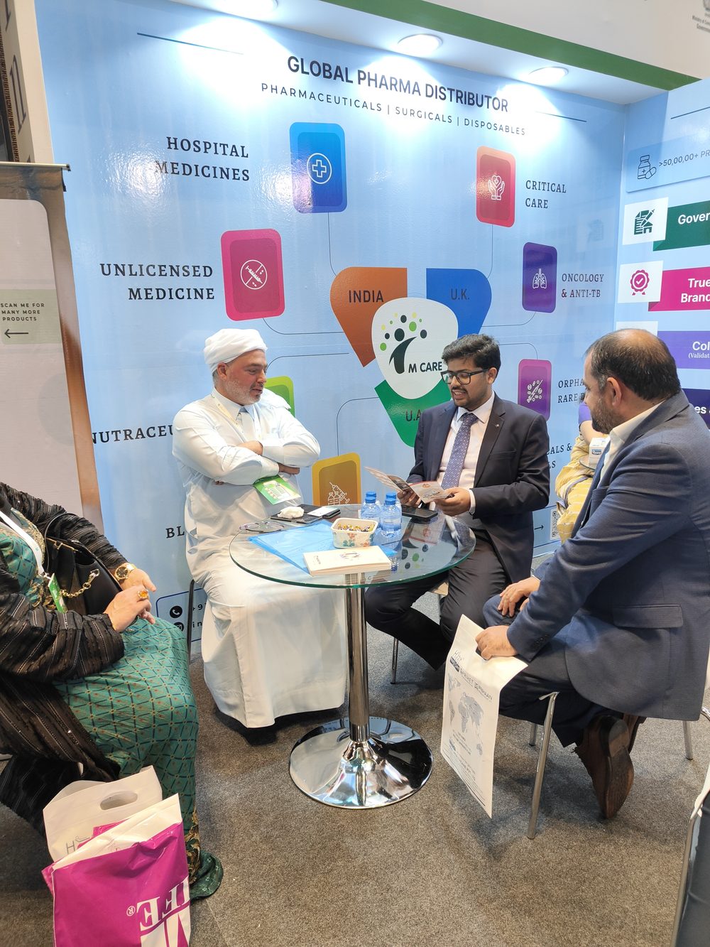 M Care Arab Health 2025 booth, "Global Pharma Distributor" banner, buyer meeting in progress.